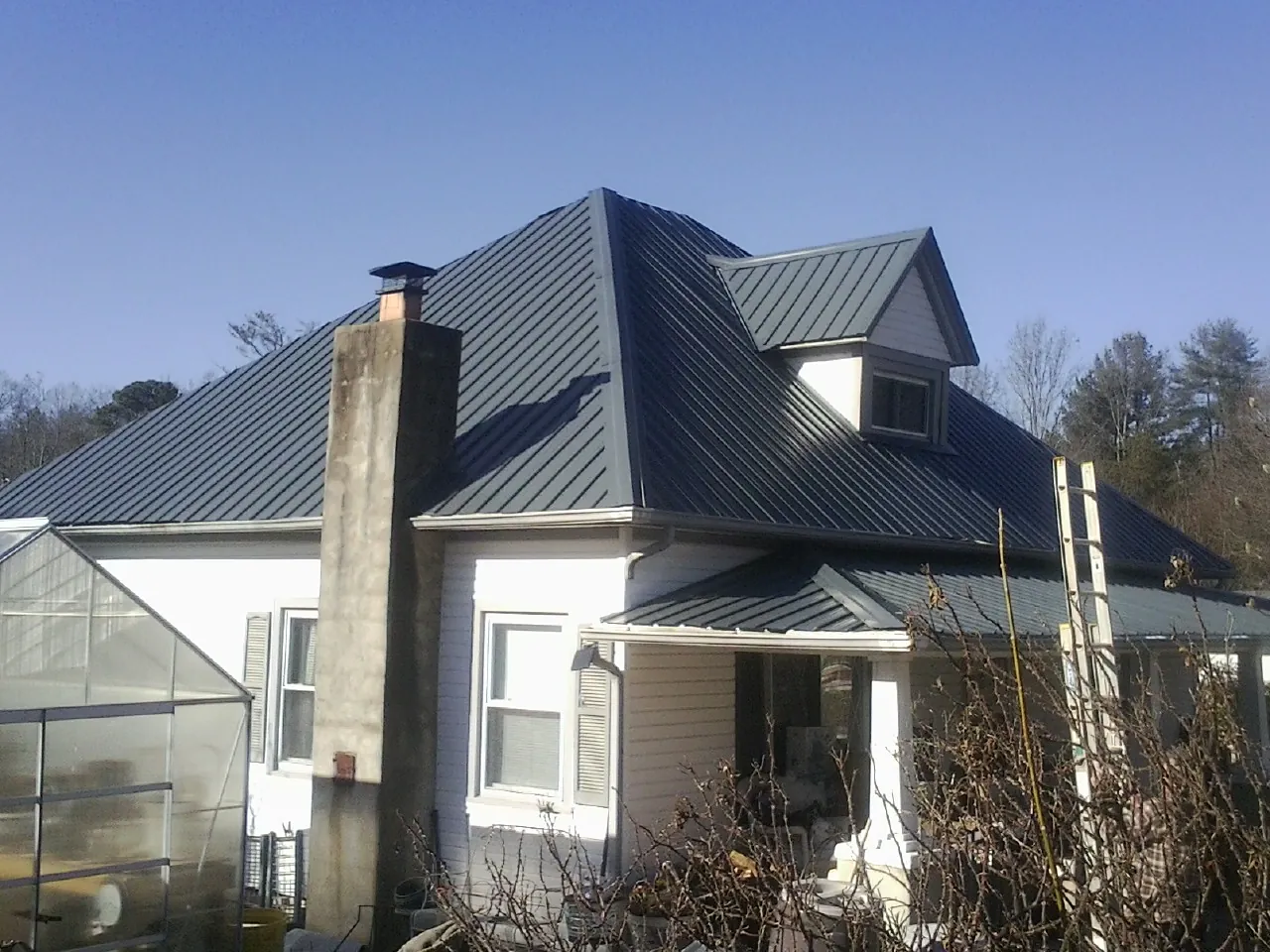Dark blue standing seam metal roof on a white farmhouse with dormer — Slate & Tile Roof Repair by Roofing Brothers in Chanute