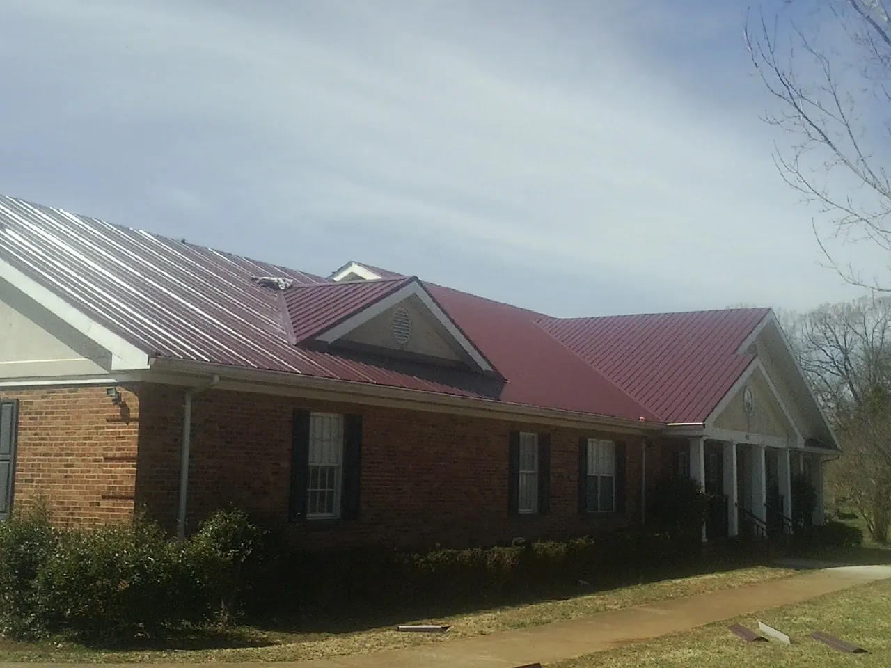 Red metal roof with gabled entries on a long brick building, from a Hail Damage Roof Repair job in Chanute