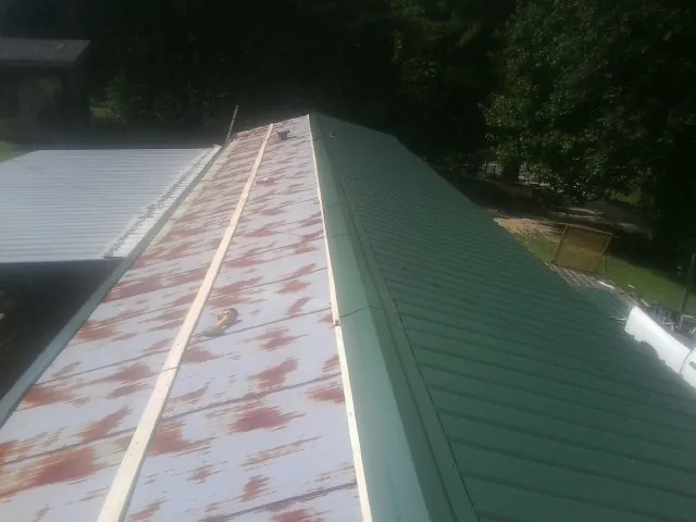 Old rusted panels beside newly installed green metal roofing — Wind Damage Roof Repair by Roofing Brothers in Chanute