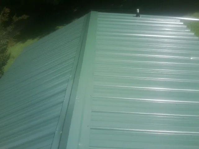 New green metal panels meeting at the ridge of a roof — Flat Roof Repair work by our crew in Chanute