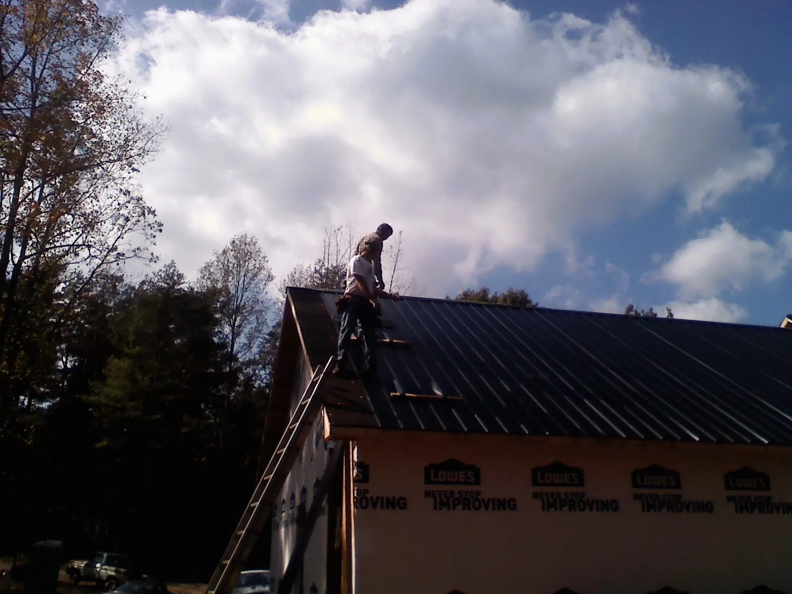 Roofer fastening dark metal panels high against a cloudy sky, from a Roof Inspection job in Chanute