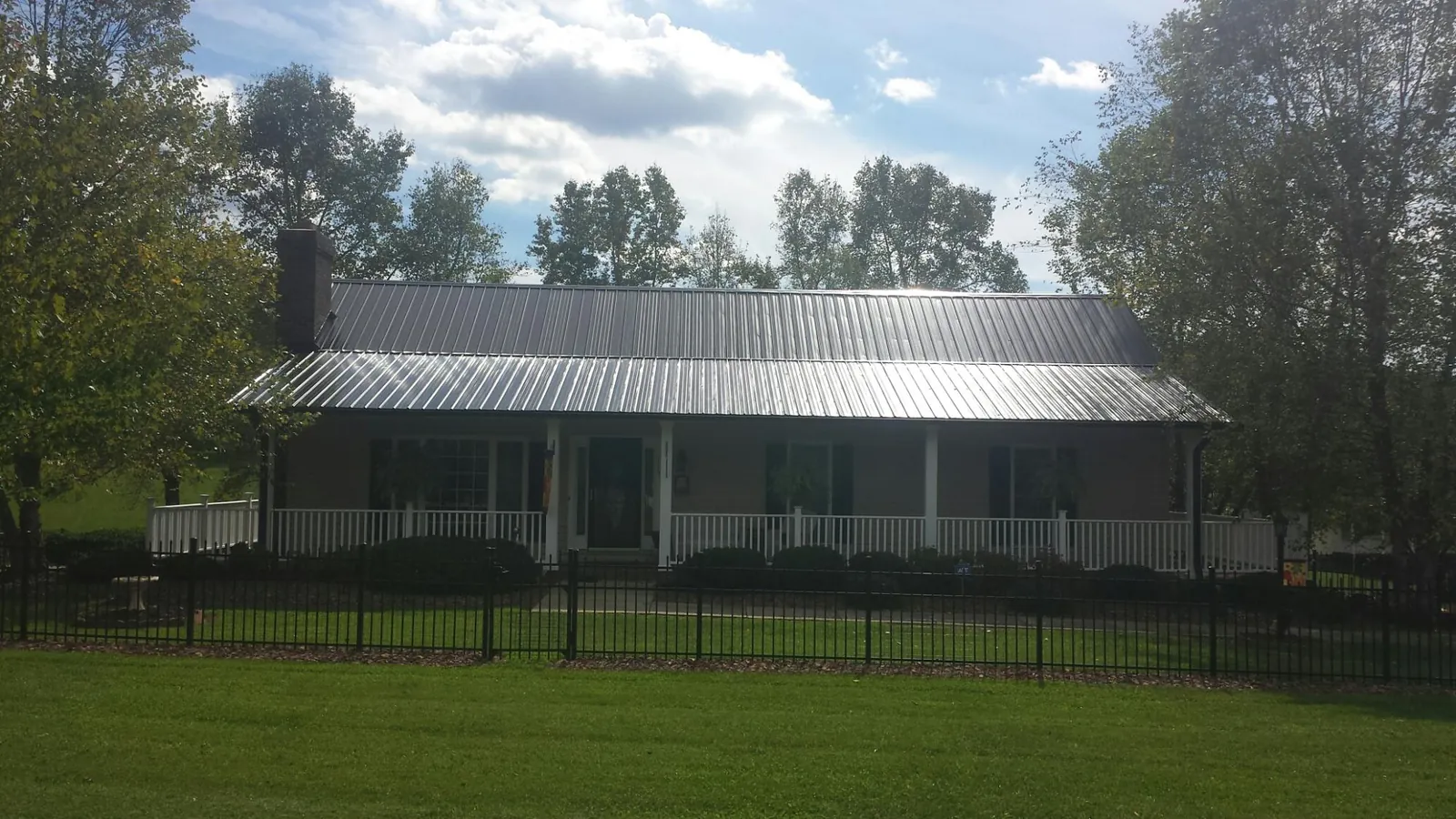 Gray metal roof on a brick ranch with a full width front porch — Gutter Guard Installation work by our crew in Chanute