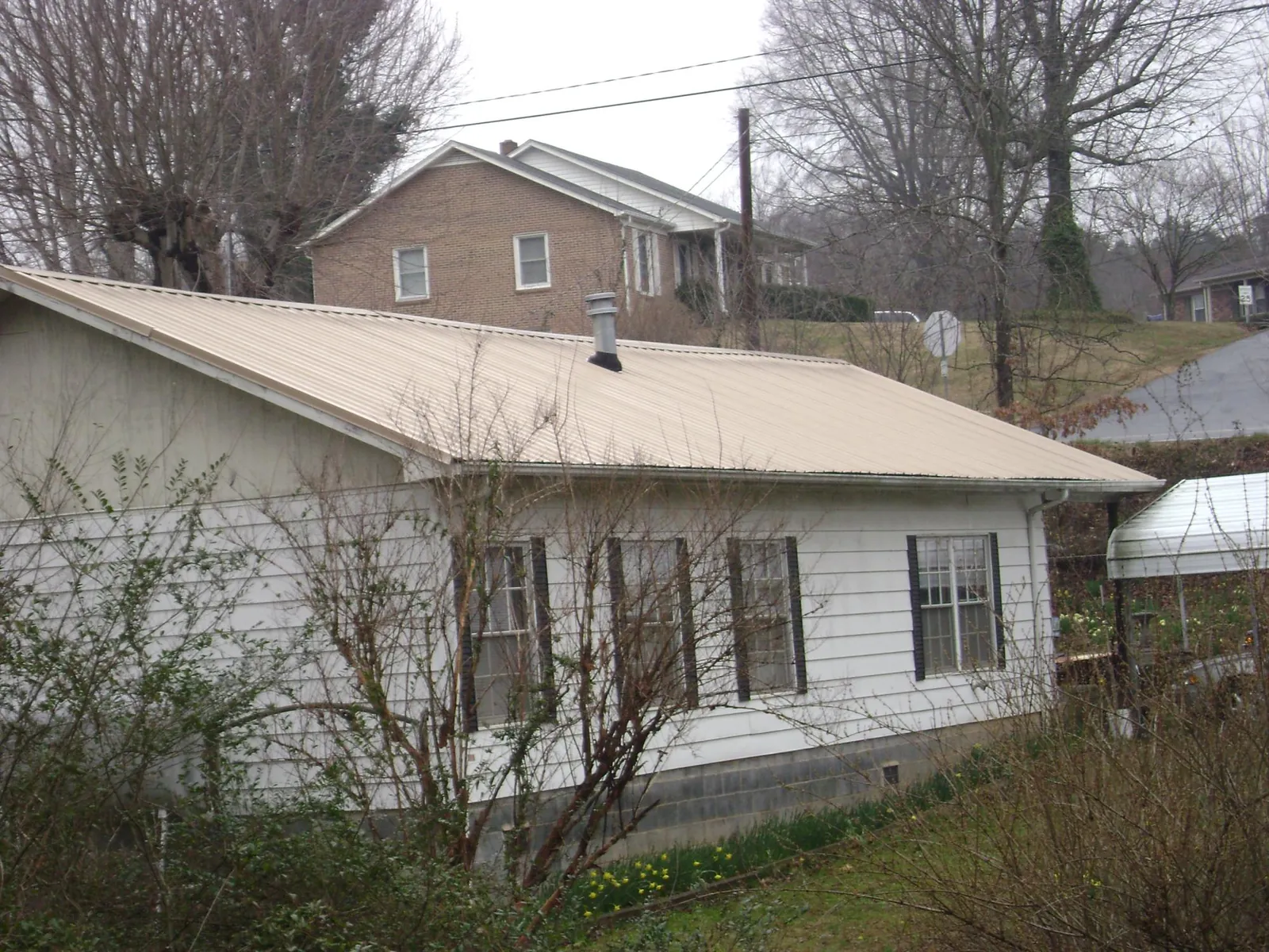 Tan metal roof on a white sided house set into a hillside — Commercial Roofing by Roofing Brothers in Chanute