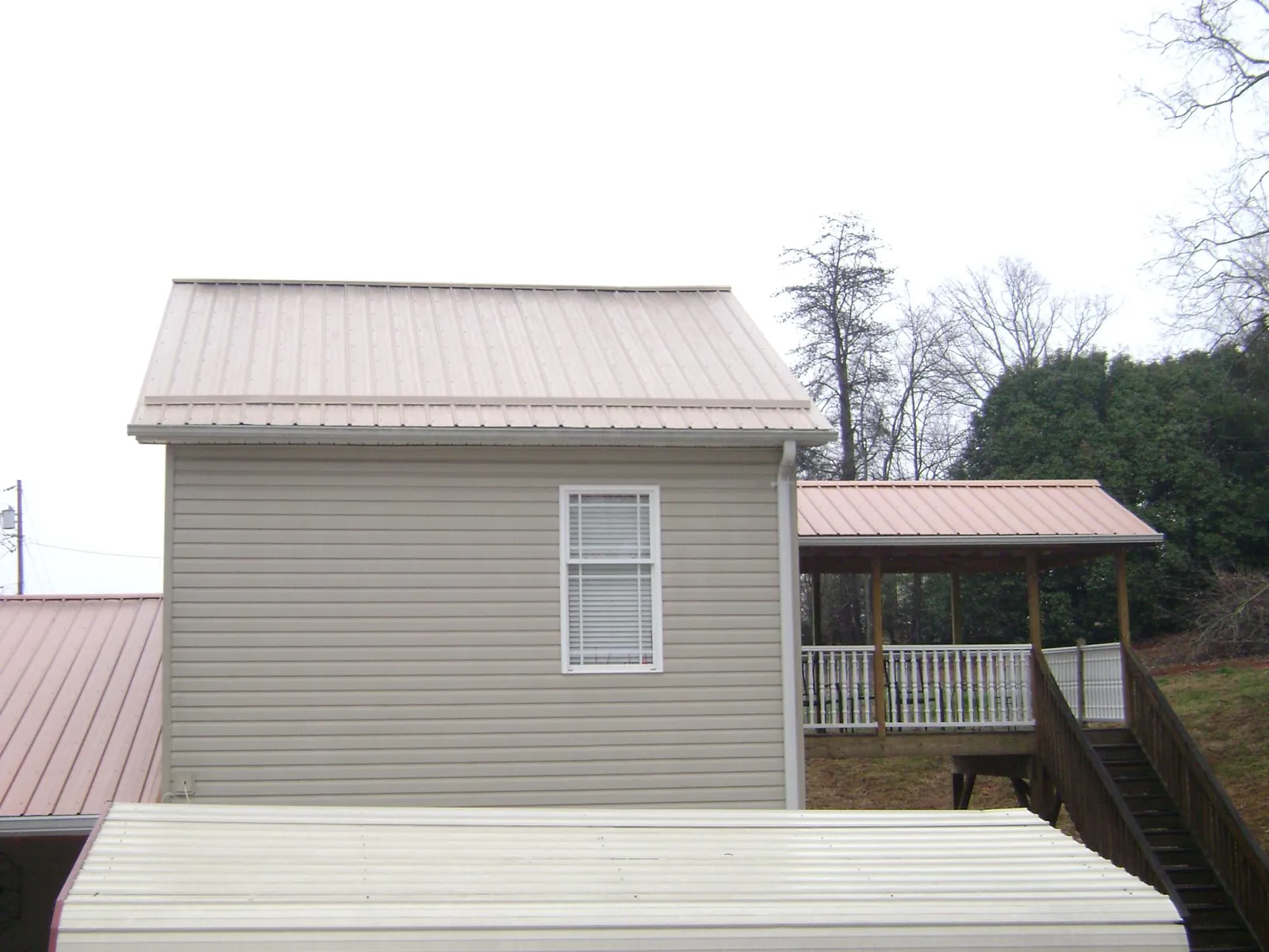 Tan metal roofs on a two story addition and attached porch, from a Roof Replacement job in Chanute